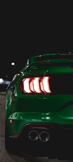 the rear end of a green sports car in a parking lot at night with its lights on