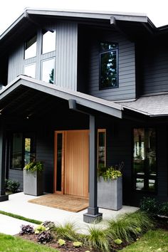 a black house with two large planters on the front porch and one door open