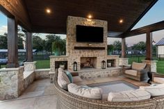 an outdoor living area with couches and a television on top of a stone fireplace