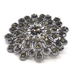 a brooch that is sitting on top of a white surface with green and yellow stones