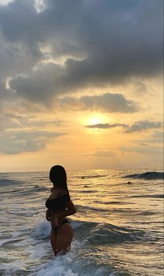 a woman standing in the ocean at sunset