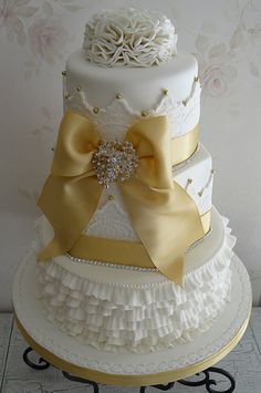 a three tiered wedding cake with yellow ribbons and bows on the top, sitting on a metal stand