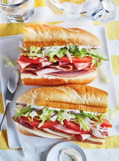 two sub sandwiches with meat, lettuce and tomato on a white platter