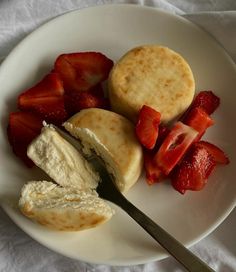 a white plate topped with pancakes and sliced strawberries next to a knife on top of a table