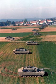 several tanks are lined up in the middle of an open field with houses in the background