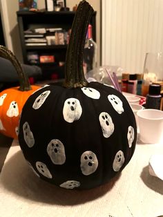 a black pumpkin decorated with white ghost faces on it's side and two orange pumpkins in the background