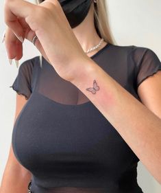 a woman with a butterfly tattoo on her left arm, wearing a black shirt and mask