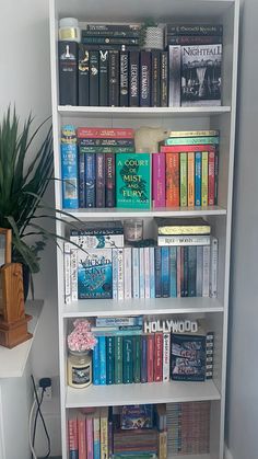 a book shelf filled with books next to a potted plant