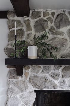 a stone fireplace with two candles and a potted plant on the mantel above it