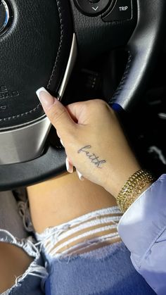 a woman with a small tattoo on her left hand is holding the steering wheel knob