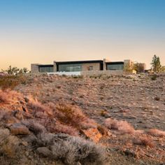 a house on top of a hill in the middle of an arid area with rocks and bushes