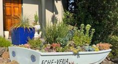 a boat shaped planter with succulents and plants in front of a house