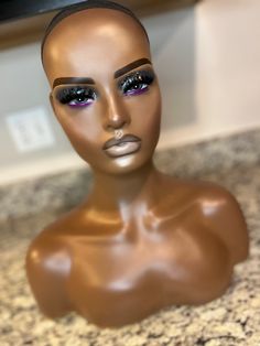 a brown mannequin head with purple eyes and black hair sitting on a counter