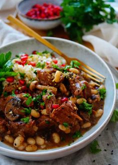 a white bowl filled with meat and beans on top of a table next to a fork