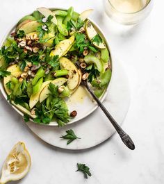 a white plate topped with salad next to a glass of water and an apple slice