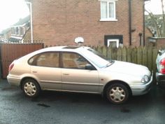 a silver car parked in front of a house next to a wooden fence and brick building