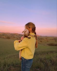 a woman holding a baby goat in her arms while standing on top of a lush green field