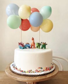 there is a cake with balloons on the top and an animal figurine in the middle