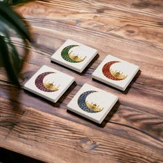 four wooden coasters with designs on them sitting on a table next to a potted plant