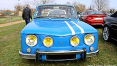 an old blue car parked on top of a grass covered field next to other cars