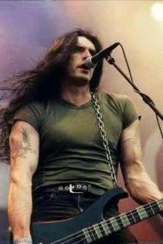 a man with long hair holding a guitar in front of a microphone and wearing a green shirt