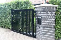 a brick fence and gate in front of a house with green bushes on either side