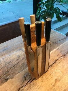 three knives in a wooden holder on a table next to a potted plant and window