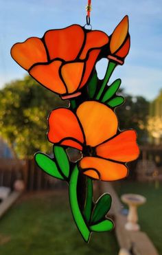 a stained glass sun catcher with orange flowers hanging from it's side in a yard