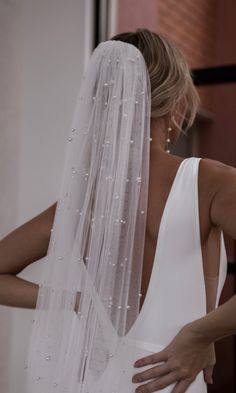 a woman in a white dress is wearing a wedding veil with pearls on the side