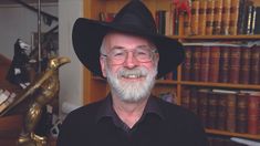 an older man wearing a black hat and glasses in front of bookshelves,