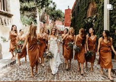 a group of bridesmaids walking down a cobblestone street in brown dresses