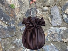 a hand holding a brown purse in front of a stone wall