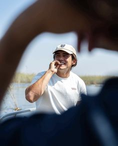 a man brushing his teeth while sitting in a boat on the water with another person nearby