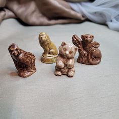 four small ceramic animals sitting on top of a bed next to each other in front of a blanket