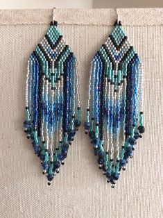 two pairs of blue and green beaded earrings hanging on a white fabric wall next to each other