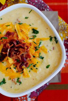 a bowl of soup with cheese and bacon in it sitting on a colorful table cloth