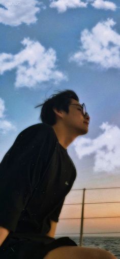 a man sitting on top of a wooden bench next to the ocean under a cloudy sky