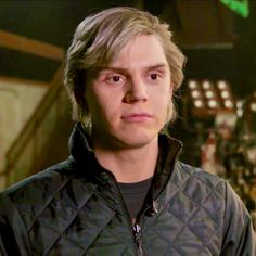 a young man with blonde hair wearing a quilted jacket and looking at the camera