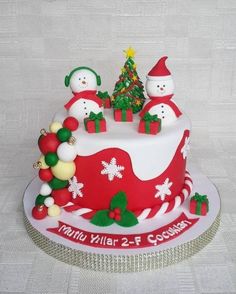 a decorated christmas cake with snowmen and trees on it's top, sitting on a white tablecloth