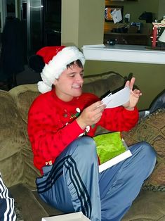 a young man sitting on top of a couch wearing a santa hat and holding a piece of paper