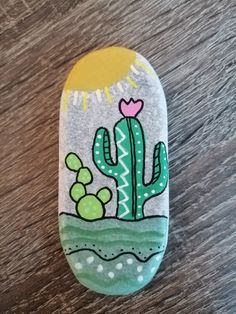 a painted rock with a cactus and sun on the top, sitting on a wooden surface