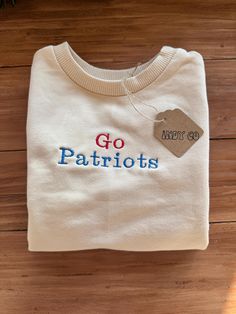 a white shirt with the words go patriots on it sitting on a wooden floor next to a potted plant