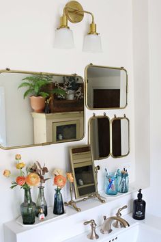 there is a sink and mirror in the bathroom with flowers on the shelf next to it