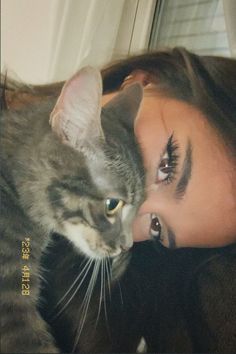 a woman laying down next to a cat with her eyes wide open and looking at the camera