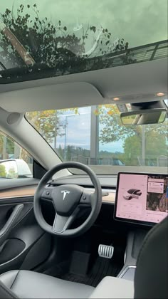 the interior of a car with dashboard, steering wheel and display screen showing an image of trees