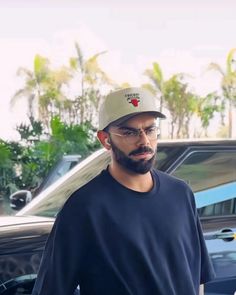 a man with glasses and a cap standing in front of a car