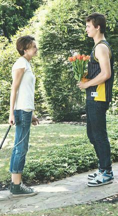 two people standing on a sidewalk talking to each other with flowers in their hands and one holding an umbrella