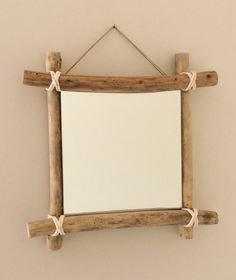 a mirror hanging on a wall with rope around the frame and wooden sticks attached to it