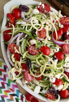 a white bowl filled with zucchini noodles and cherry tomatoes, topped with feta cheese