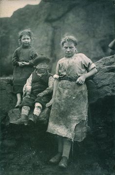 an old black and white photo of three children standing next to each other in front of a rock formation